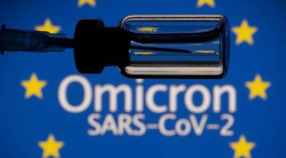 A vial and a syringe are seen in front of a displayed EU flag and words Omicron 2
